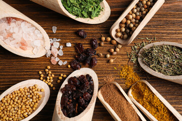 Scoops with different spices on wooden table, flat lay