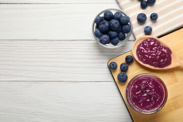 Delicious blueberry jam and fresh berries on white wooden table, flat lay. Space for text