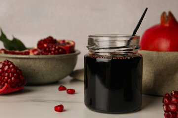 Glass jar of tasty pomegranate sauce on white marble table. Space for text