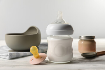 Bottle of milk and pacifier on white wooden table