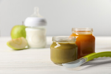Jars with healthy baby food and spoon on white wooden table. Space for text