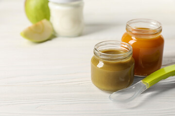 Jars with healthy baby food and spoon on white wooden table. Space for text
