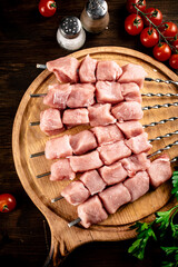 Pork kebab raw on skewers with parsley and tomatoes on a cutting board. 