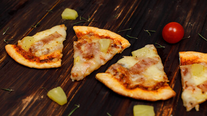 Closeup top view studio shot four pieces of hot oven baked tasty delicious Italian homemade ham and pineapple traditional Hawaiian soft bread crust pizza decorated on wooden table with tomatoes herbs