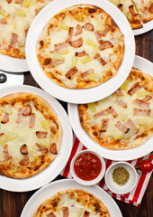 Closeup top view studio shot of multiple hot oven baked tasty delicious Italian homemade ham pineapple traditional Hawaiian bread crust pizzas placed on white dishes ready to serve in restaurant