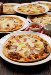 Closeup top view studio shot of multiple hot oven baked tasty delicious Italian homemade ham pineapple traditional Hawaiian bread crust pizzas placed on white dishes ready to serve in restaurant