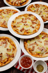 Closeup top view studio shot of multiple hot oven baked tasty delicious Italian homemade ham pineapple traditional Hawaiian bread crust pizzas placed on white dishes ready to serve in restaurant