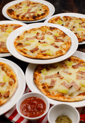 Closeup top view studio shot of multiple hot oven baked tasty delicious Italian homemade ham pineapple traditional Hawaiian bread crust pizzas placed on white dishes ready to serve in restaurant