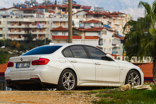 Alanya, Turkey – April 17 2021:  white  BMW 3-series 320i  is parked  on the street in city against the backdrop of a buildung,  shops