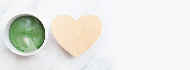 Banner with gel eye mask and an empty wooden heart. Flat lay. Top view. Concept of caring for the skin under the eyes. Copy space. Cosmetic product. Place for text.