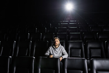 A man drinks coffee while watching a movie at the cinema