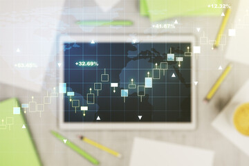 Abstract creative financial graph with world map and modern digital tablet on desktop on background, top view, financial and trading concept. Multiexposure