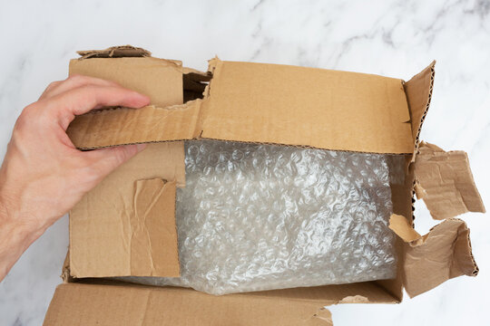 Man opens a damaged and torn cardboard box to transport things. Top view. Bubble wrap keeps things and utensils in transit.