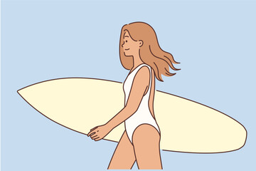 A surfer girl walks holding a surfboard in her hands