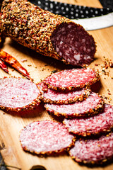 Pieces of salami sausage on a cutting board with pods of dried chili peppers. 