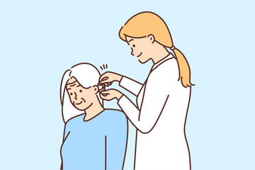 Female doctor install hearing aid to old patient 