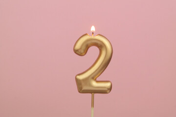 Burning golden birthday candle on pink background, number 2