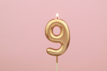 Golden birthday candle shaped as number 9 on pink background