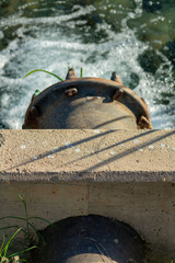 Cement retaining wall near river or industrial water reserve with black metal pipe pumping fluids and liquids