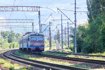 Obraz premium An old electric train on the railway tracks enters the city on a summer sunny day.