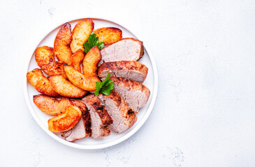 Baked pork tenderloin with quince or apple slices served on plate. White table background, top view