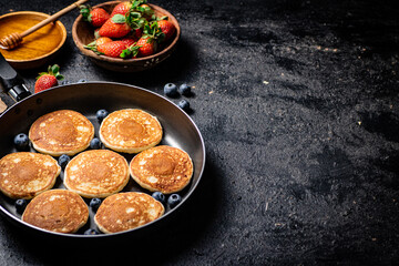 Pancakes in a frying pan with fresh berries and honey. 