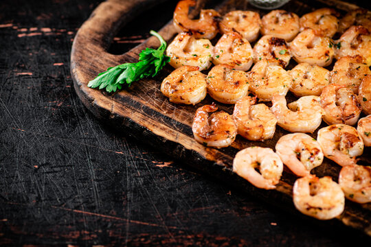 Grilled shrimp on skewers with parsley on a cutting board. 