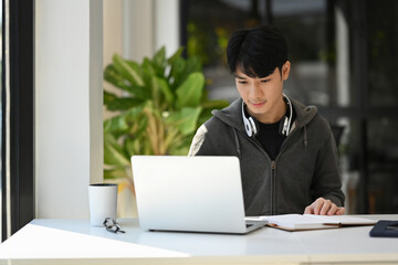 Young man freelancer in casual wear using laptop, working remotely from home