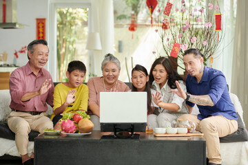 Big family gathered in front of laptop to video call relatives from another country