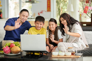 Fototapeta premium Joyful parents and children waving with hands when making video call at Tet celebration