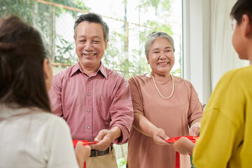 Happy senior couple giving red envelopes to grandchildren at Tet celebration