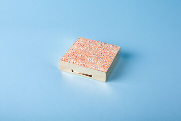 Closed Eyeshadow palette for make-up on blue background. Classic Eyeshadow palette with facial mirror. Closed metallic box with shining rhinestones on the top.