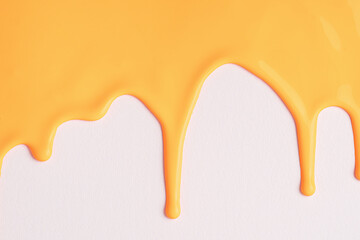 Orange liquid drops of paint color flow down on white canvas. Abstract art. Yellow paint dripping on the white wall with copy space.