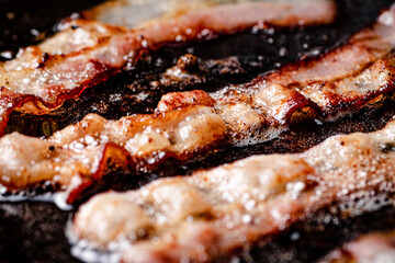 Pieces of bacon are fried in boiling oil with air bubbles. 