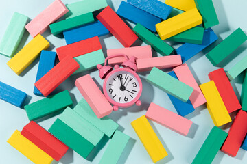 demolished jenga tower made of color wooden blocks and a pink clock on light blue background