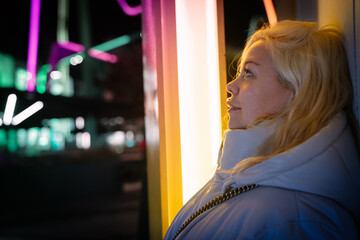 Blonde young woman walking at night and leaning against the wall while having a satisfied half smile on her face