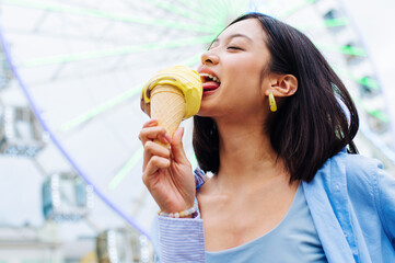 Beautiful young asian woman eating ice cream at amusement park - Cheerful chinese female portrait during summertime vacation- Leisure, people and lifestyle concepts