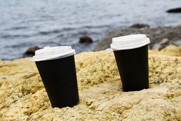 Two paper cups for coffee stand at a distance from each other on a stone against the background of...