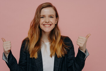 Happy ginger young girl in formal jacket showing thumbs up with both hands