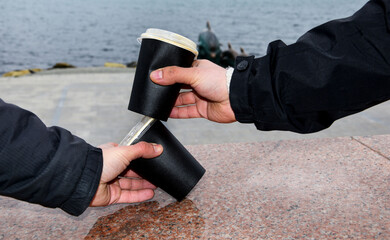 Two paper coffee cups stand on a marble border. Male hands take glasses of coffee against the background of the blue sea. Takeaway cup with lid with ready drink. Recycling of used material, recreation