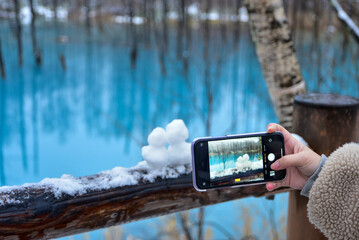 青い池で作った雪だるまをスマホで撮影する女子