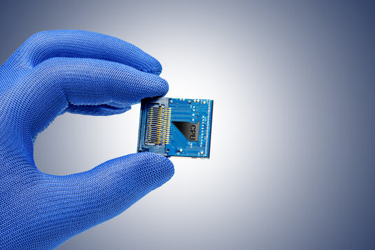 hand holds a cpu against the grey blue background.  Concept of production or repair electronic chips, pc system. Selective focus.