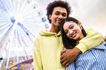 Multiracial young couple of lovers dating at theferry wheel in the amusement park - People with mixed races having fun outdoors in the city- Friendship, releationship and lifestyle concepts