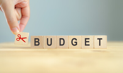 Cutting budget strategy. Reducing expenses to maintain financial stability, help businesses achieve  financial goals and stay profitable. Using scissors to cutting word budget on wooden cube blocks.