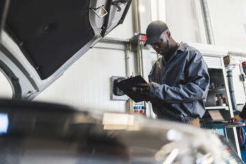 Medium shot of a black mechanic checking things on his pad. Blurred foreground. Repair shop...