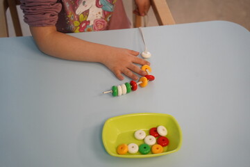 Almaty, Kazakhstan - 10.12.2022 : The child's hand is on the table next to the educational game beads for motor skills.