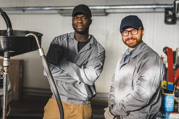 Mechanics posing for the camera while changing engine oil in an auto repair shop. High-quality photo