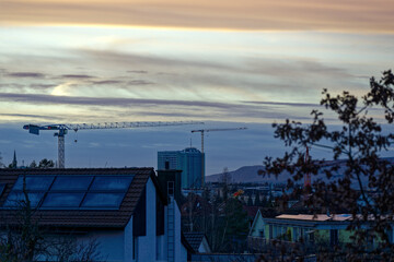 Rooftops at City of Zürich district Schwamendingen with crane and beautiful colorful evening winter sky in the background. Photo taken January 10th, 2023, Zurich, Switzerland.