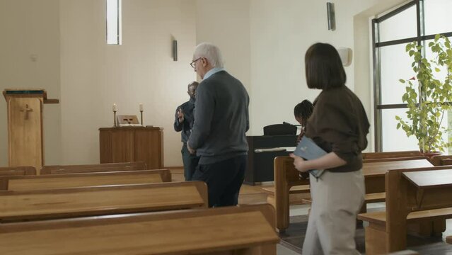 Young adult African American priest greeting people attending Sunday service in Catholic church