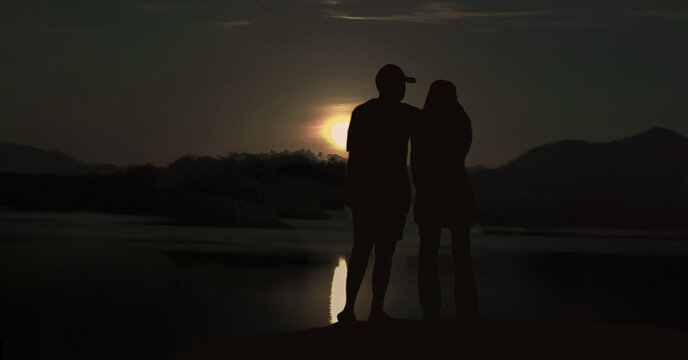 silhouette of a couple standing by the water at dusk